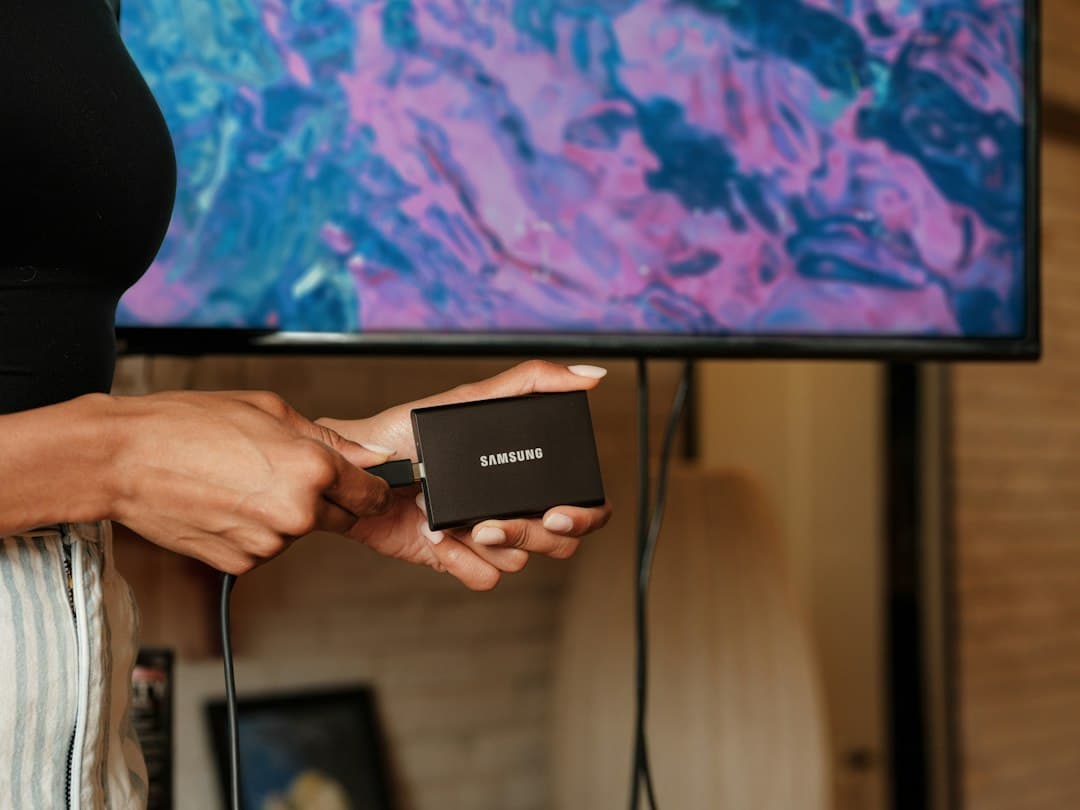 Télécommande Fire TV Stick tenue devant un téléviseur allumé